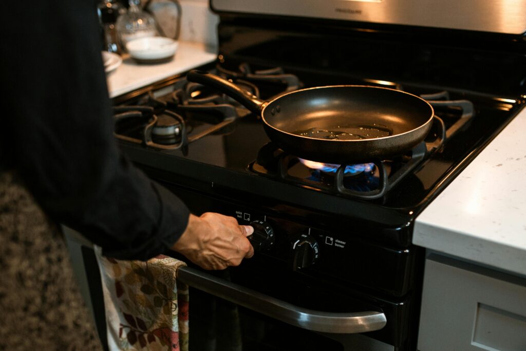 pexels-photo-4910217-4910217 A person in a modern kitchen adjusting the stove dial under a frying pan on a gas burner.